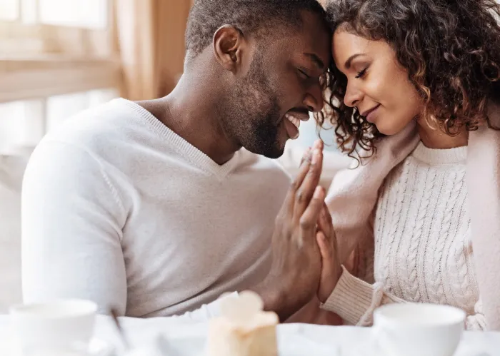 Peacefulness in us. Delighted peaceful positive African American couple sitting in the cafe and touching hands of each other while expressing peacefulness and love