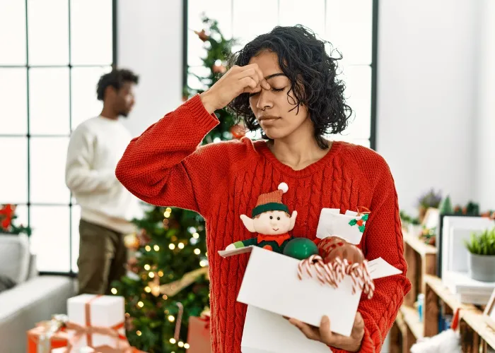 Young hispanic woman standing by christmas tree with decoration tired rubbing nose and eyes feeling fatigue and headache. stress and frustration concept.