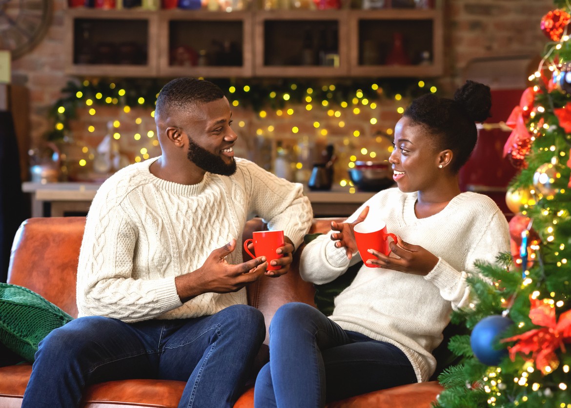 Romantic african american couple celebrating Christmas eve together at home, drinking hot chocolate and chatting