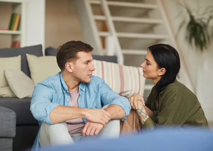 Warm toned portrait of modern young couple talking to each other sincerely while sitting on floor in cozy home interior, copy space