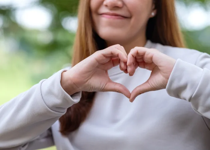 Closeup image of a young woman making heart hand sign